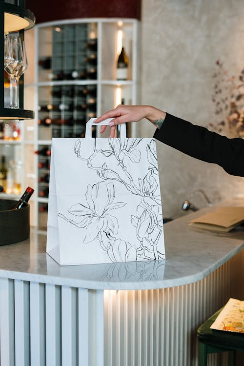 a woman is holding a white paper bag with a floral pattern on it