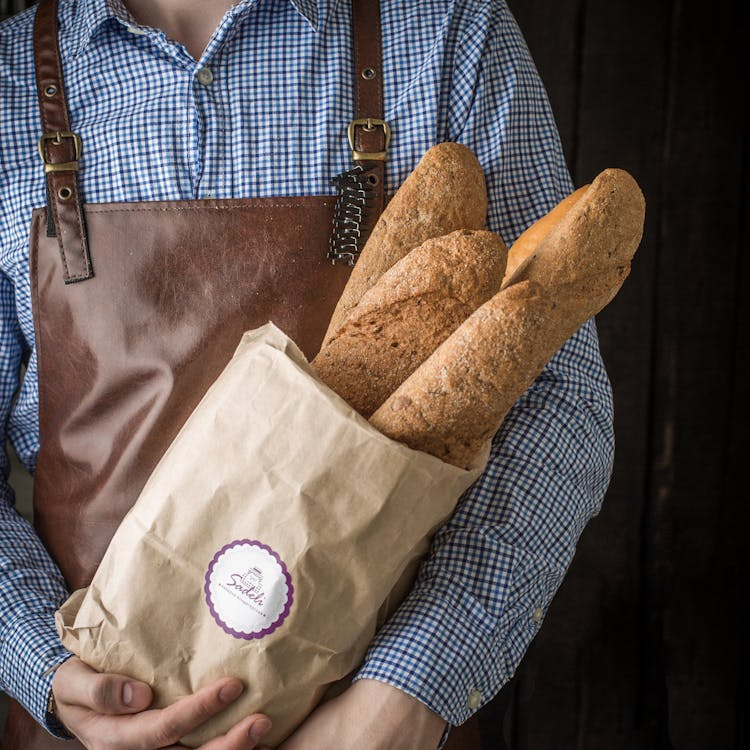 A person is holding a bag full of bread loaves 