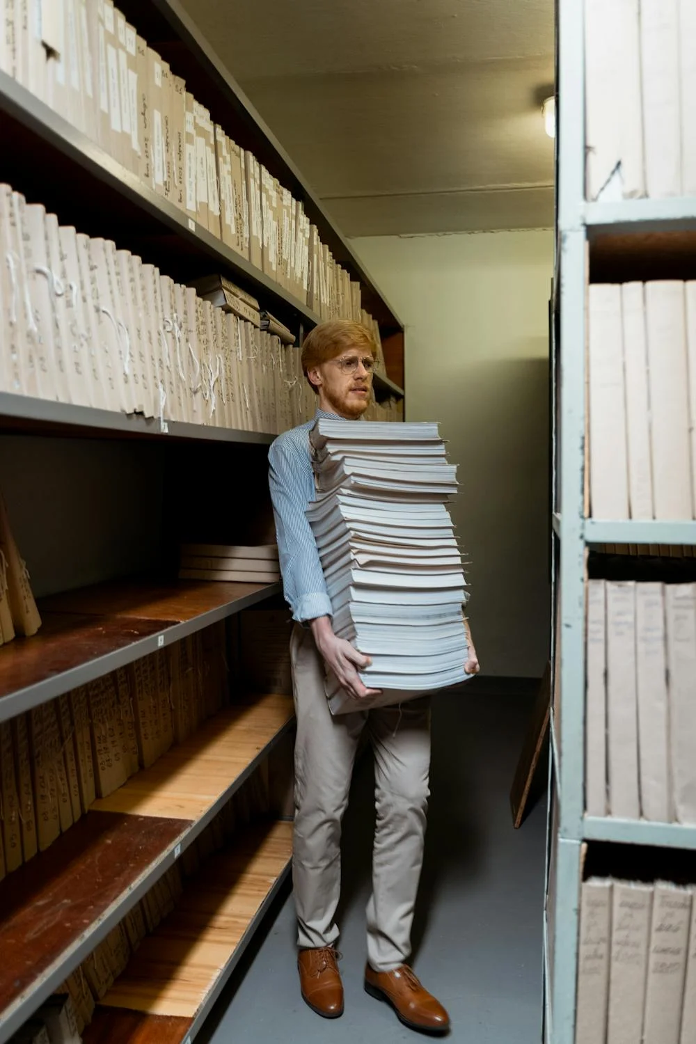 A person lifting multiple reams of printer paper bundled together.