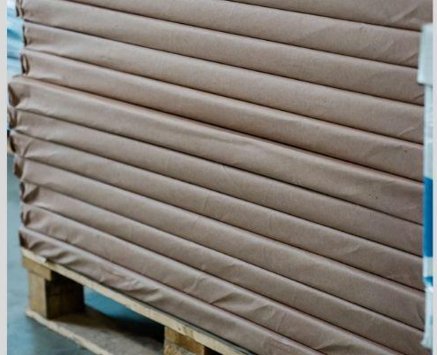 Stack of large brown-wrapped paper sheets on a wooden pallet, prepared for bulk shipping from a paper supplier in the UAE.
