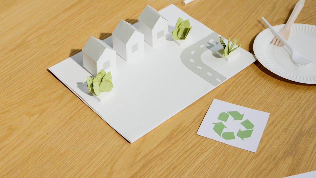 An image of a paper model of a neighborhood set on a table along with paper plates, disposable forks, and a photo of a recycling symbol.