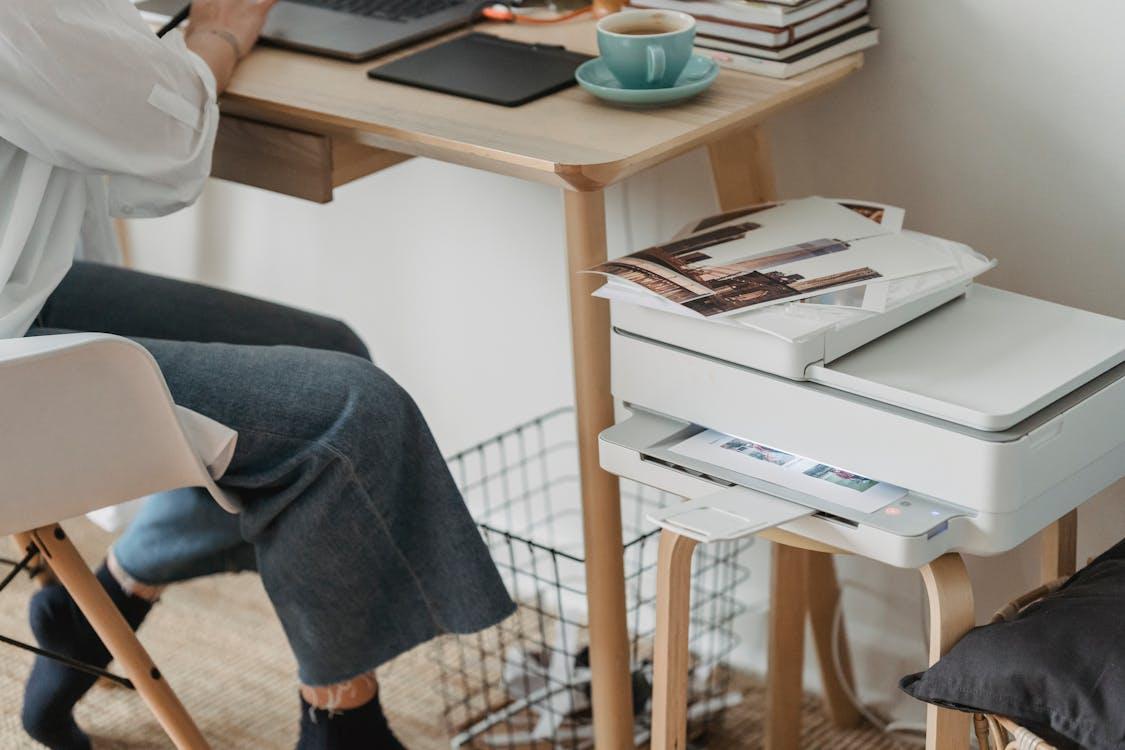 A woman working on her desk with a printer by her side, printing pictures on A4-size paper Image caption