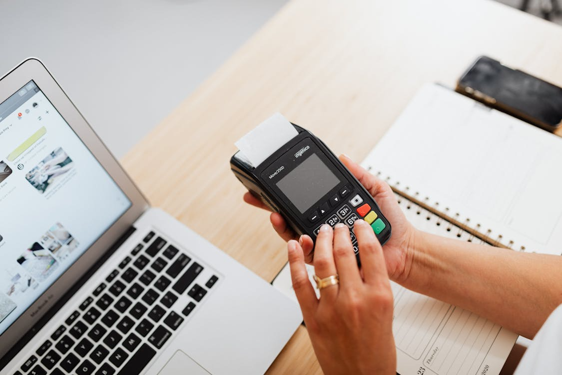 Individual holding a black digital device near an ATM for banking transactions.